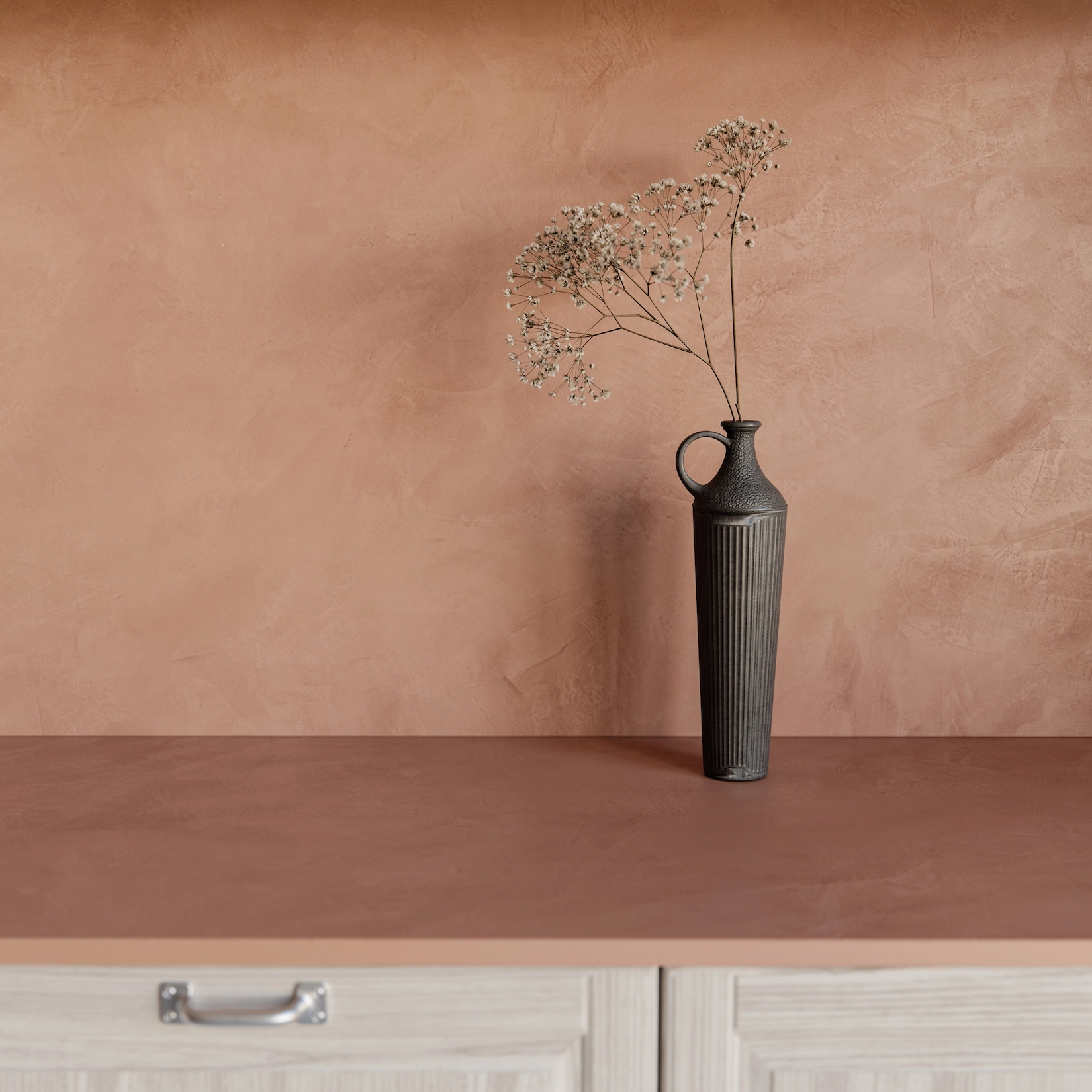 Terracotta plaster wall with vase above shaker cabinetry